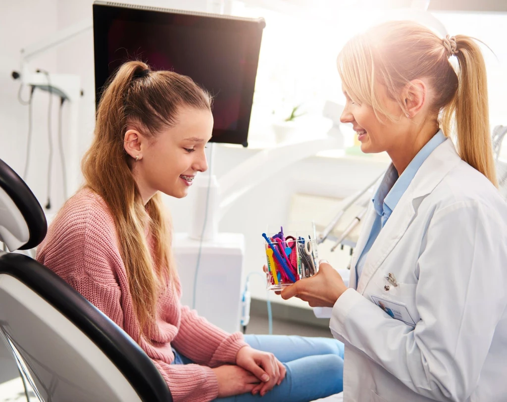 Orthodontist talking with a smiling girl in the treatment chair